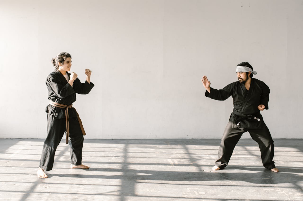 Two martial artists practice self-defense in a bright, empty room.